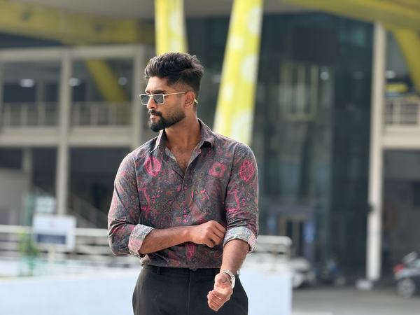 Eswar in a paisley shirt and sunglasses in front of yellow pillars
