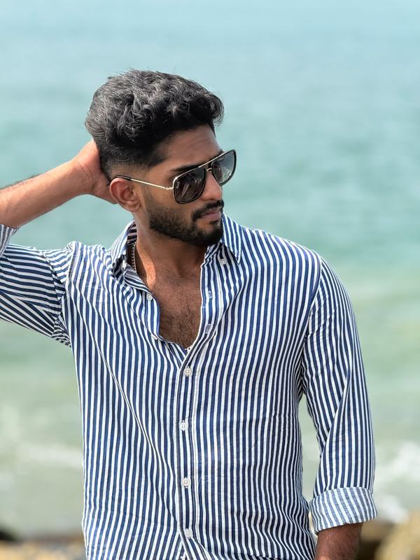 Eswar in a blue striped shirt and aviators by the sea