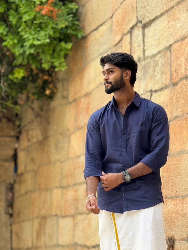 Eswar in a navy shirt and white veshti against a sandstone wall